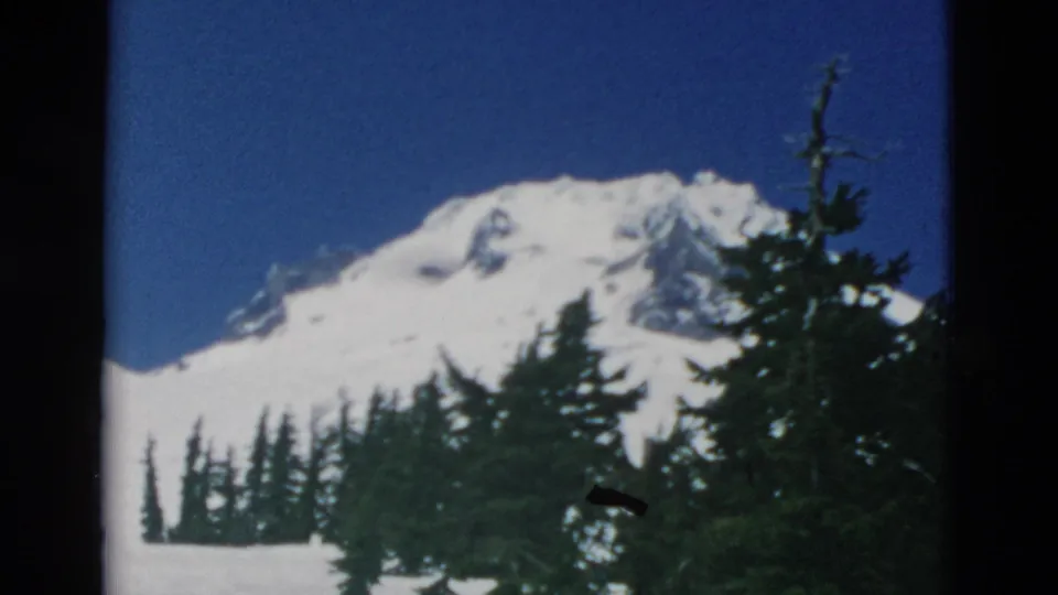 1958 Oregon 8mm frame with a snow-covered peak, evergreen foreground, blue sky, and visible film gate edges.