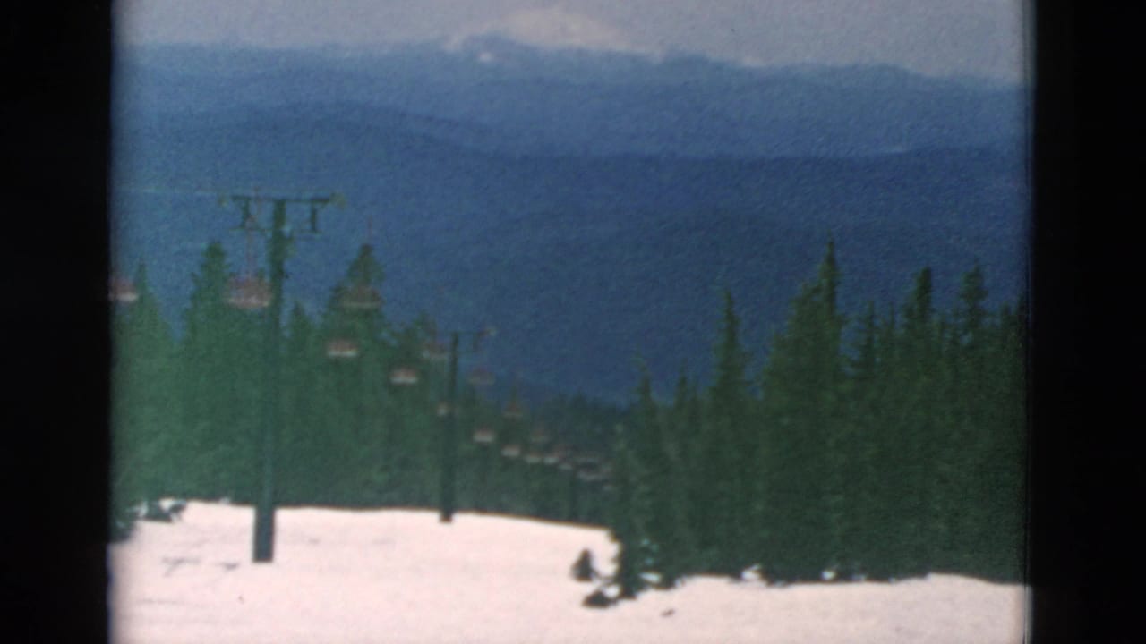 Snowy slope, chairlift line, evergreen trees, and distant blue mountain ridges.
