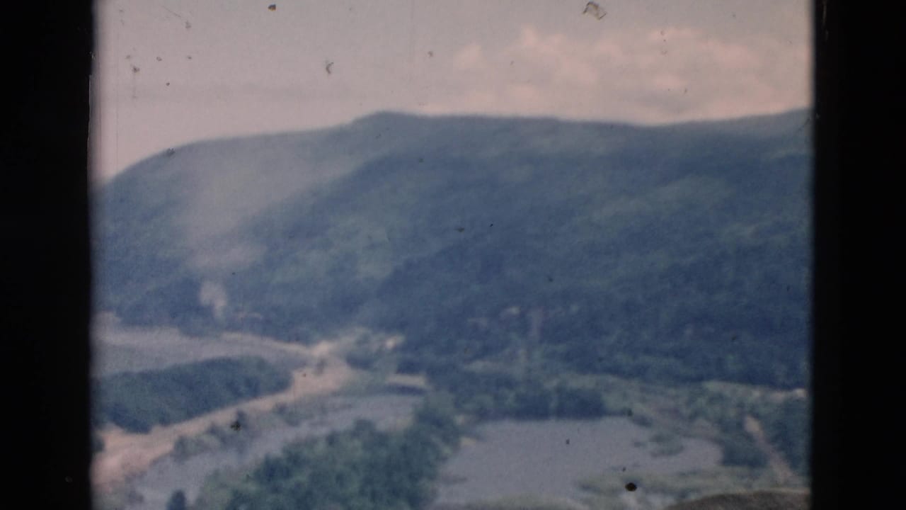 Faded color 8mm frame showing a wooded mountain valley with a winding waterway under a pale sky.