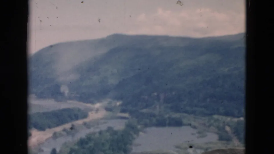 Faded color 8mm frame showing a wooded mountain valley with a winding waterway under a pale sky.