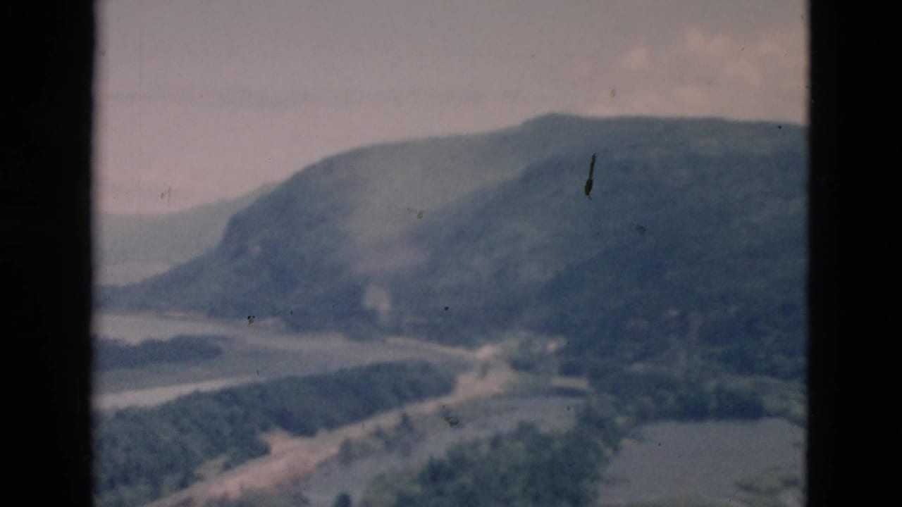 Home-movie frame with dark gate borders around a soft view of mountains, water, and wooded shoreline.