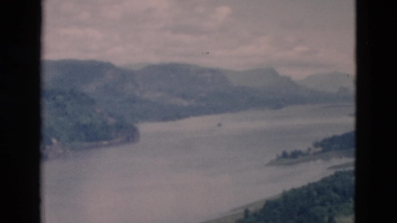 Lake bend with wooded hills and distant mountains under a hazy sky.