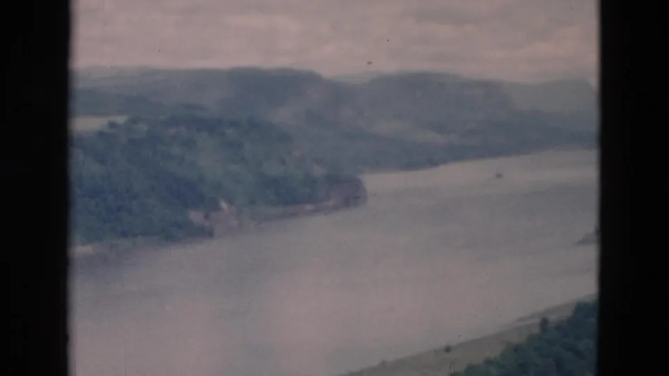 Soft 8mm frame looking over a lake edge and wooded hillside, with muted color and low-contrast haze.