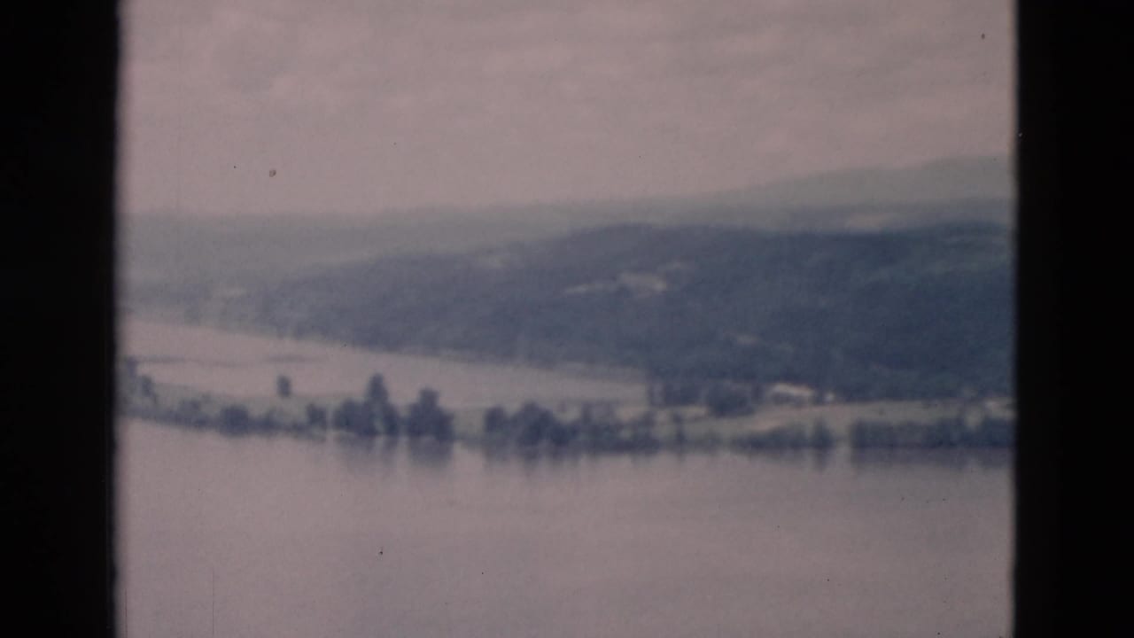 Soft 8mm view of a calm lake with distant hills and shoreline trees.