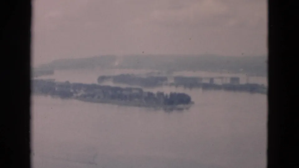 Faded 1950s 8mm frame showing a wide river, elongated island, distant shoreline, and soft horizon from a high vantage point.