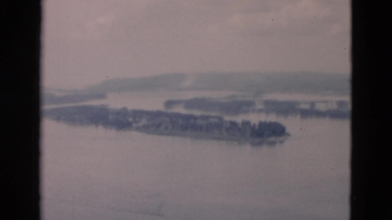 Hazy river view with wooded islands and distant low hills.