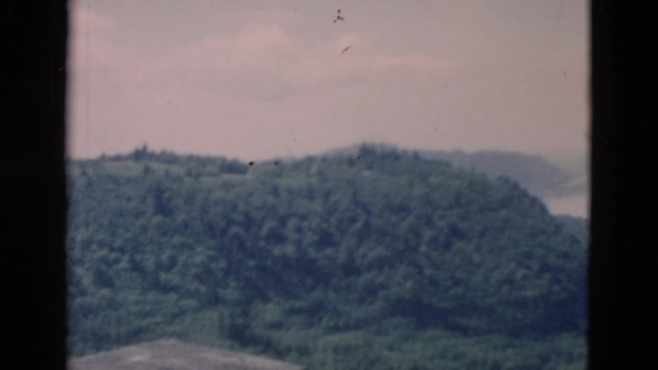 Forested hills above a broad body of water, framed by dark 8mm film borders.