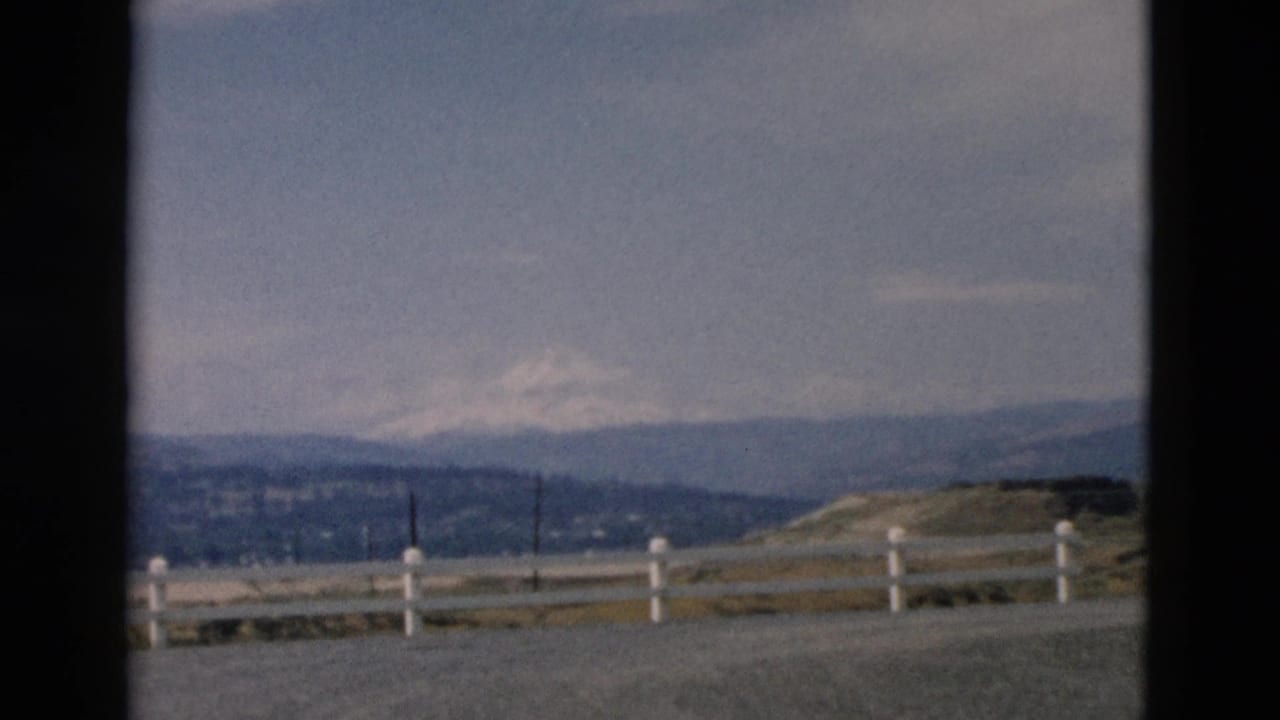 Distant mountain landscape with a white fence and cloudy sky.
