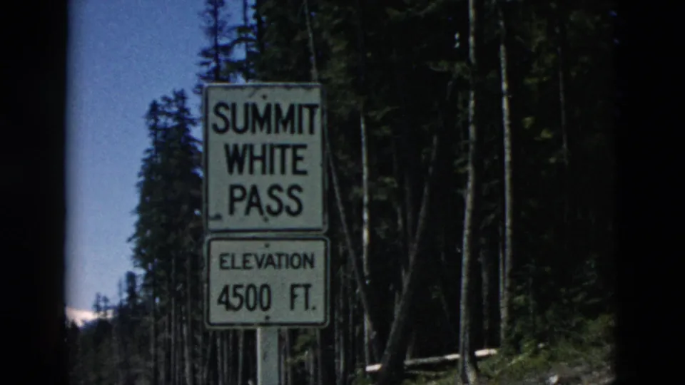 1958 8mm frame showing a Summit White Pass sign with 4500 ft elevation text beside tall conifer trees.