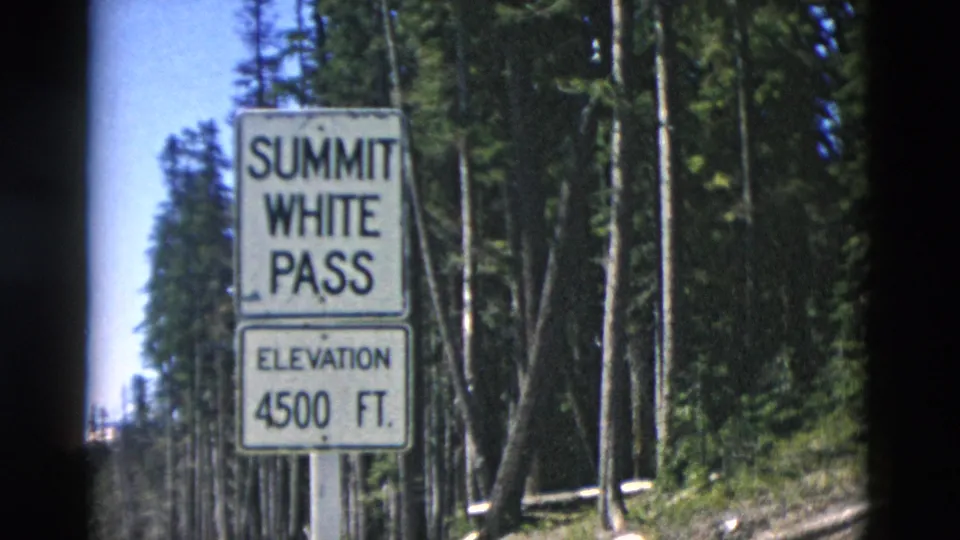 1958 8mm frame showing a Summit White Pass sign marked 4500 ft beside tall trees on a mountain roadside.