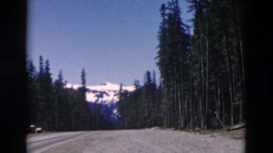 Final 1958 8mm frame looking along a mountain road toward a snow-covered ridge, with evergreens on both sides.