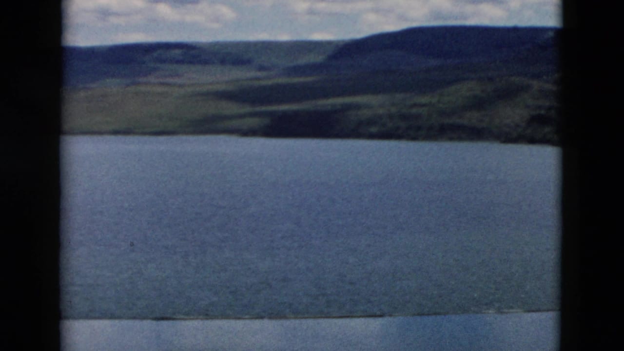 Broad blue lake with distant green hills and a partly cloudy sky.