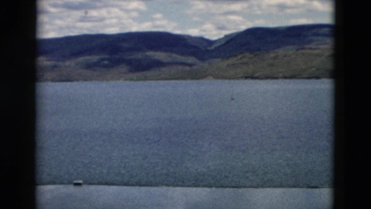 Broad lake surface with distant mountain slopes and cloudy sky.