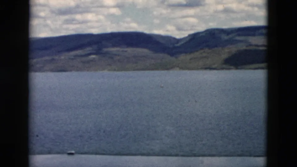 1958 Montana 8mm frame with open water, distant hills, mountain ridges, cloud cover, and dark film borders from the contact sheet scan.