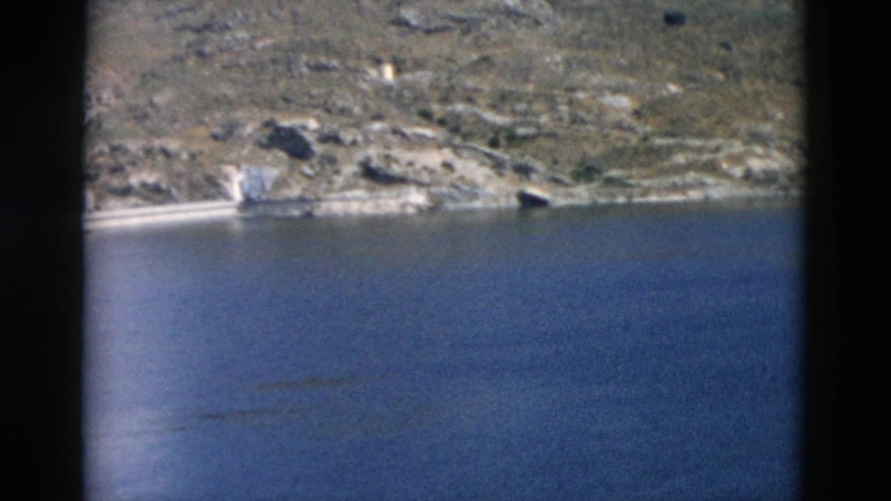 1958 Montana lake view with arid rocky hills, pale shoreline features, and blue water filling the foreground.