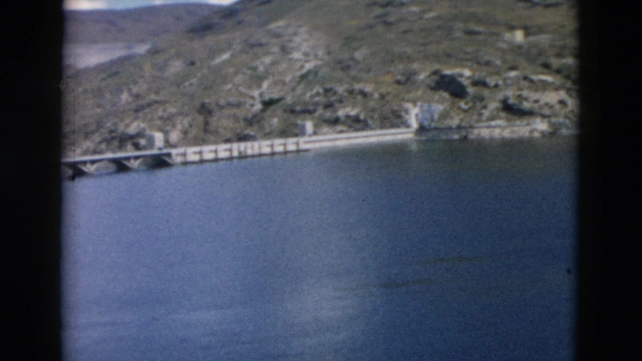 Long concrete span crosses blue water below rocky hillsides.