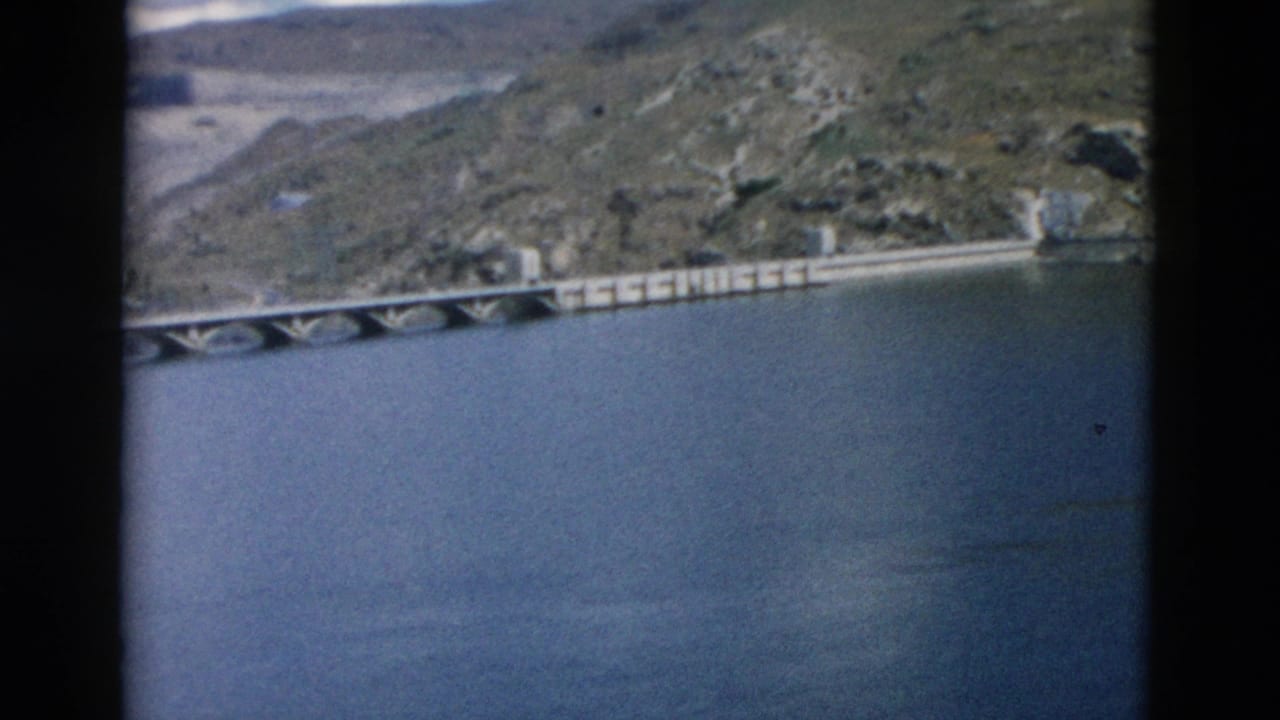 Concrete bridge continues across water with arid hills behind it.