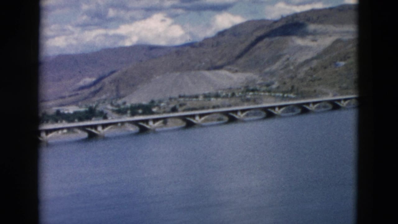 Wide river with arched bridge, hills, and partly cloudy sky.