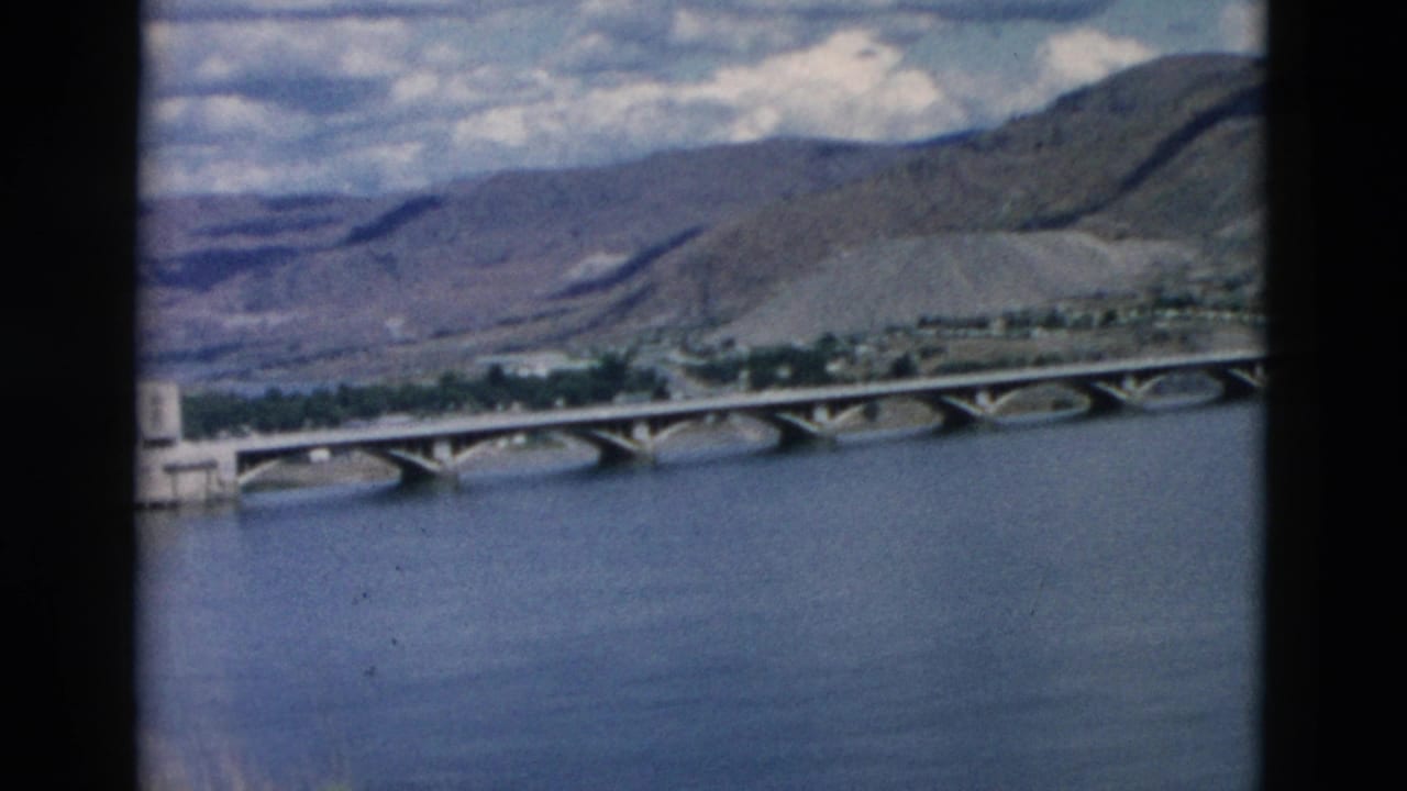 Bridge over river with mountain slope and distant shoreline trees.