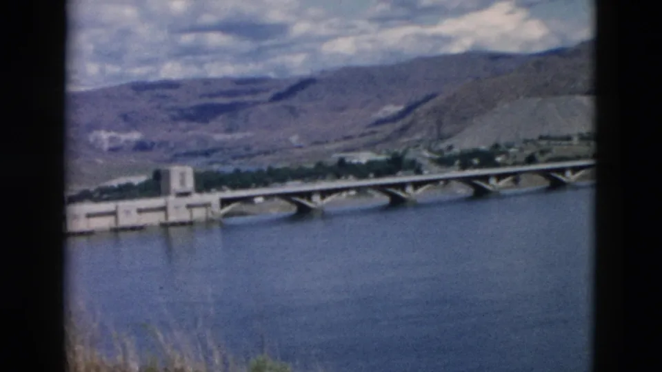 1958 Montana 8mm frame with a concrete dam or riverside structure beside the arched bridge and broad river.