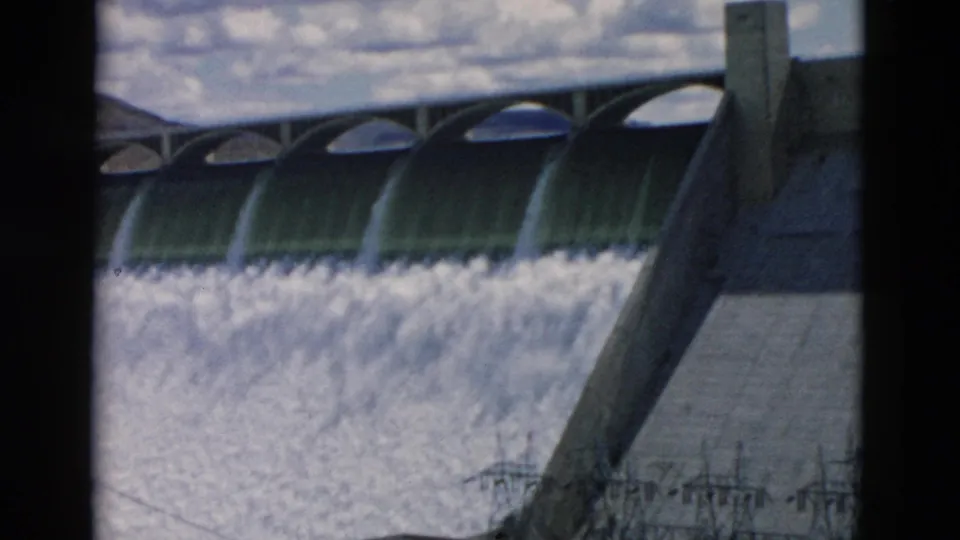 1958 Montana 8mm frame showing water cascading over a concrete dam spillway with arched spans and a structural support.