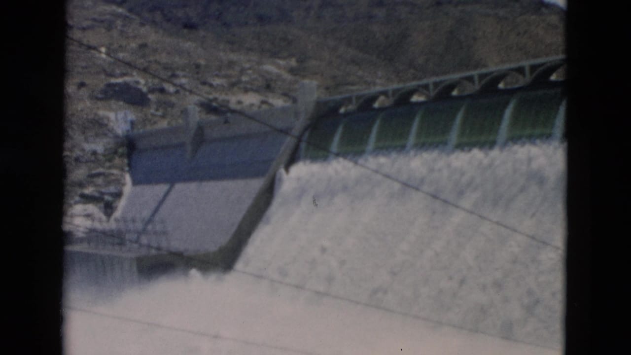 Concrete dam spillway releasing water beside a rocky hillside.