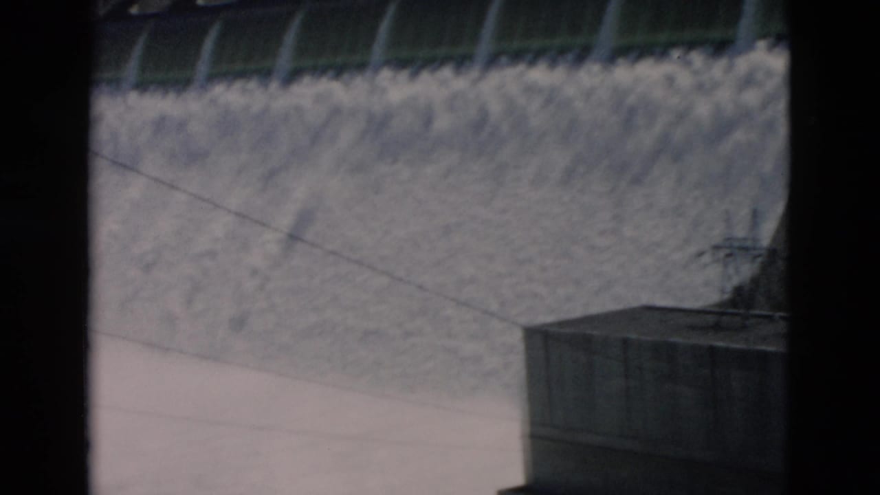 Water spills over a concrete dam with dark film borders visible.
