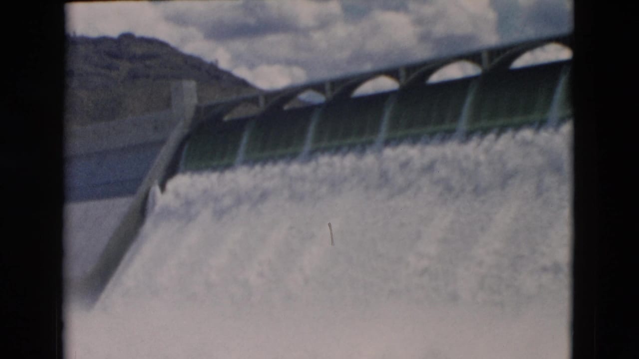 Dam spillway with arched openings and heavy water flow across the frame.