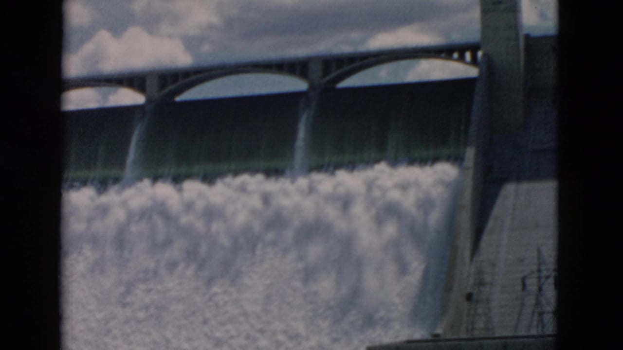 Dam spillway releasing heavy white water beneath arched gates.