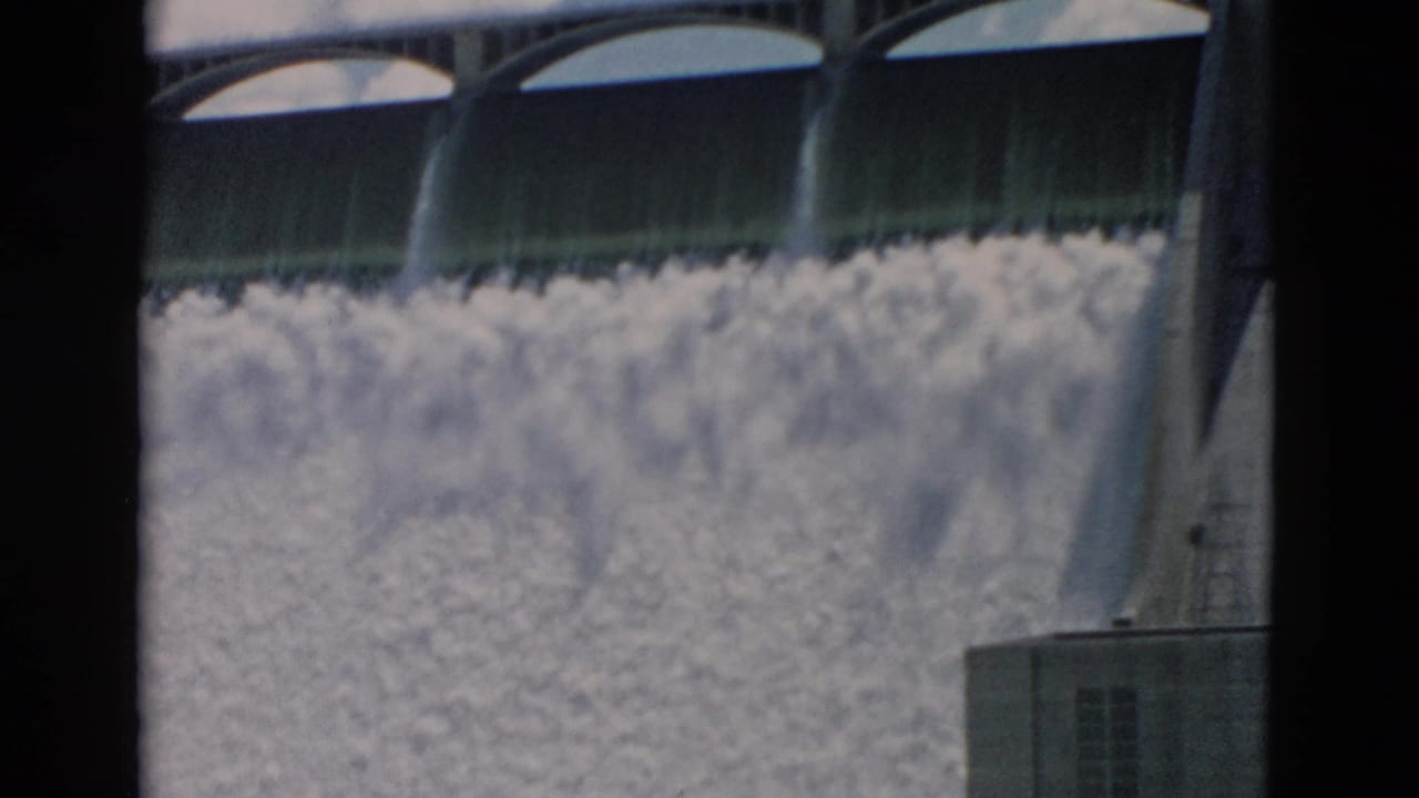 Closer view of dam gates, concrete supports, and rushing spillway water.
