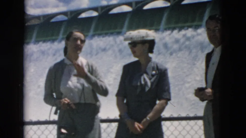 Two women and a partially seen man stand at a Montana overlook with a broad spillway or waterfall behind them.