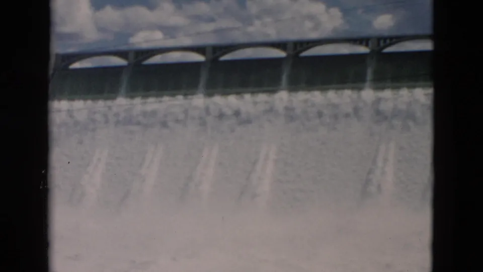 1958 Montana 8mm frame focusing on the dam structure, arched spillway openings, and cascading water with no people visible.