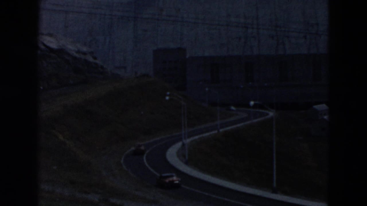 A dark view of a winding road near a large concrete dam structure.