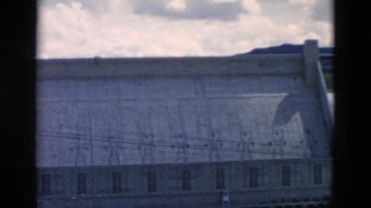 Concrete dam section with spillway edge, utility lines, and dark film gate border.