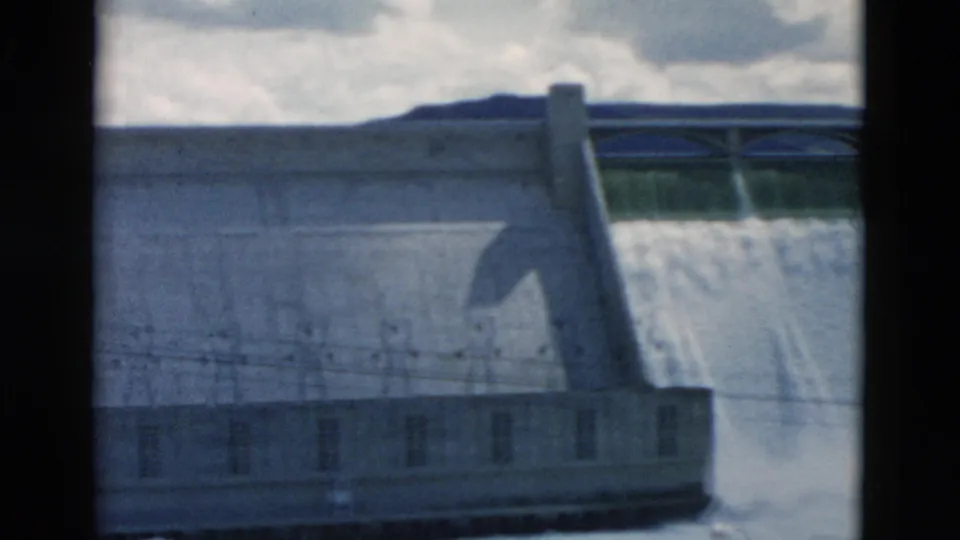 1958 Montana 8mm frame showing water pouring over the dam spillway beside a concrete wall, with wires and mist visible.
