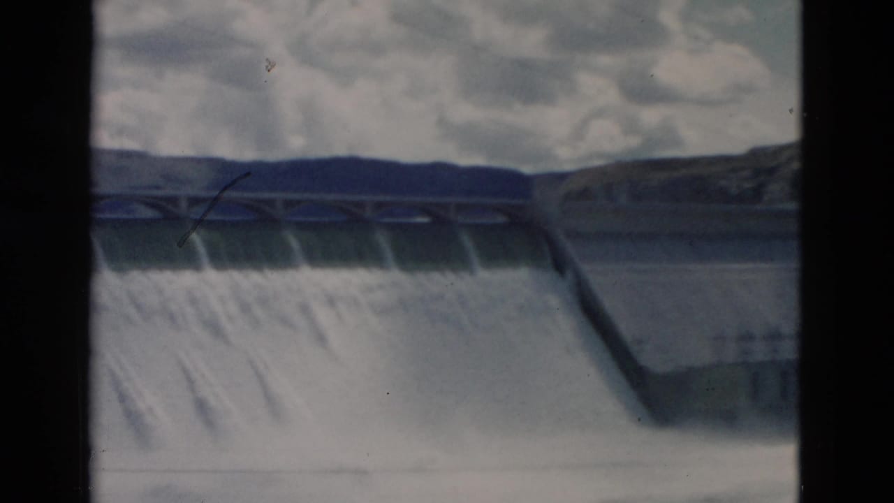 Wide view of dam spillway water with a dark film-frame divider.