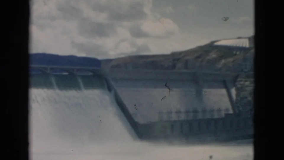 1958 Montana 8mm frame with a concrete dam spillway, water spray, hillside terrain, and a small structure above the dam.