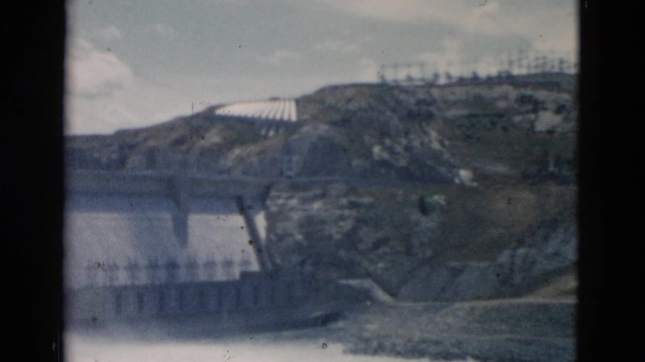 Wide view of a concrete dam or bridge structure in a rocky mountain valley with water below.