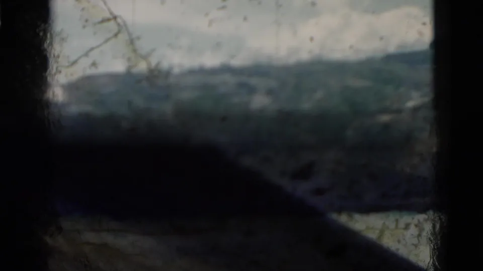 Obscured 1958 Montana home-movie frame looking across a mountain valley, partly blocked by a dark foreground shape and thin branches.