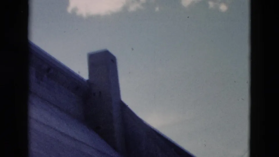 1958 Montana 8mm frame with a low-angle view of a built structural edge and vertical projection set against pale sky.