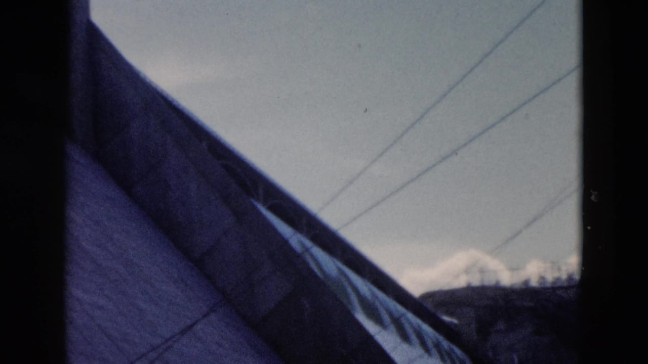 1958 Montana view past a steep roof toward power lines, dark hills, and snow-capped mountains.