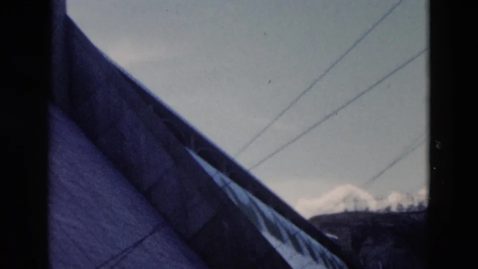 1958 Montana view past a steep roof toward power lines, dark hills, and snow-capped mountains.