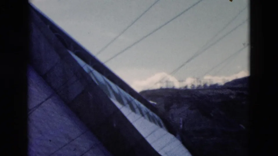 1958 Montana 8mm frame with a steep roof in the foreground and snowy mountains beyond the hills.