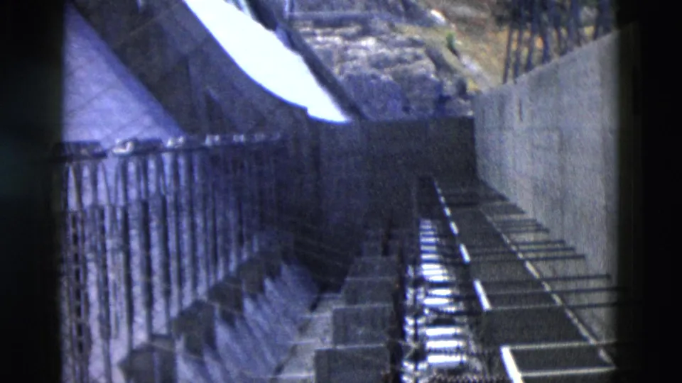 1958 Montana 8mm frame from a visitor walkway beside railings, concrete supports, and the bright sloped spillway surface.