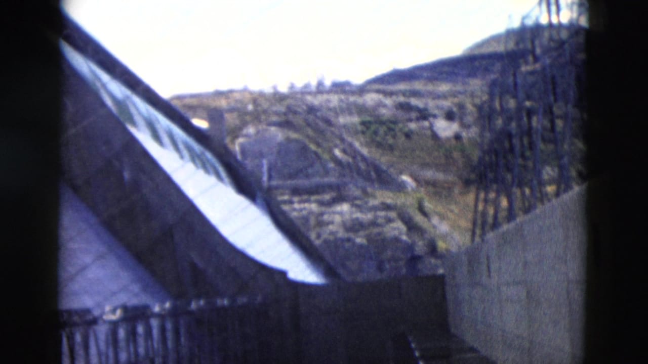 Elevated view of a hillside beside a roofline or barrier with a tall utility structure.