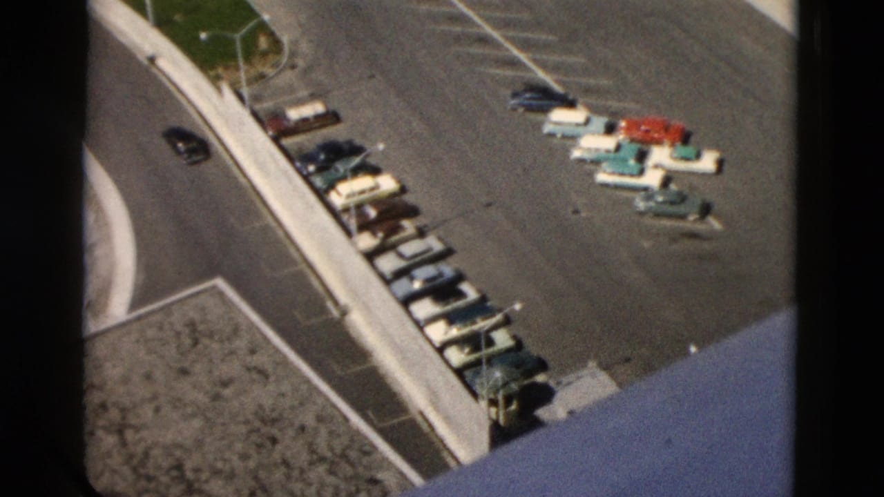 Overhead view of a parking lot with rows of vintage cars and concrete curbs.