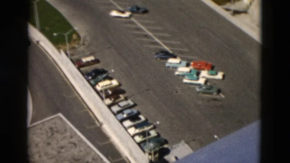 1958 Montana frame showing an angled overhead view of parked cars, painted spaces, and concrete lot edges.