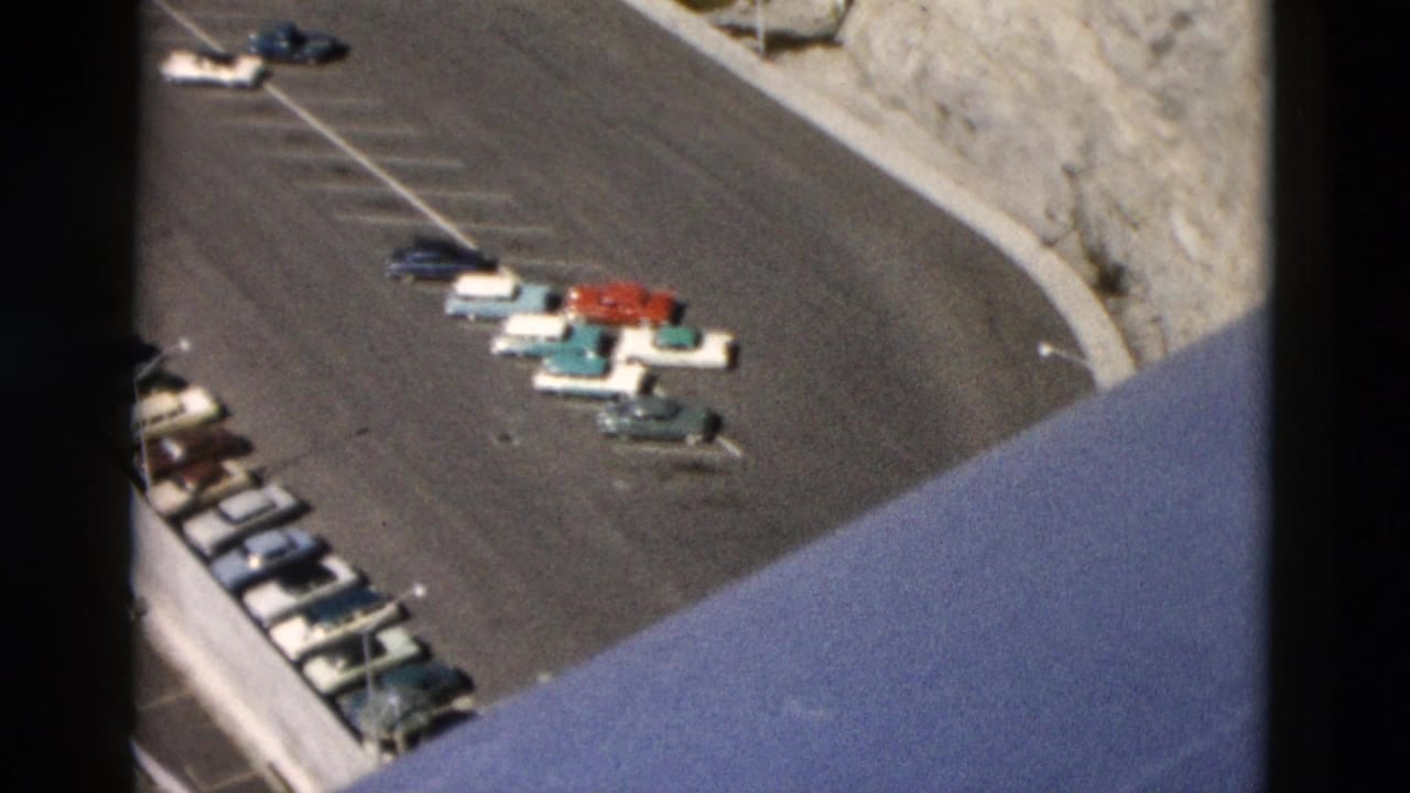 1958 Montana 8mm frame showing classic cars parked near a winding road, rocky cliff, and partial bridge structure.