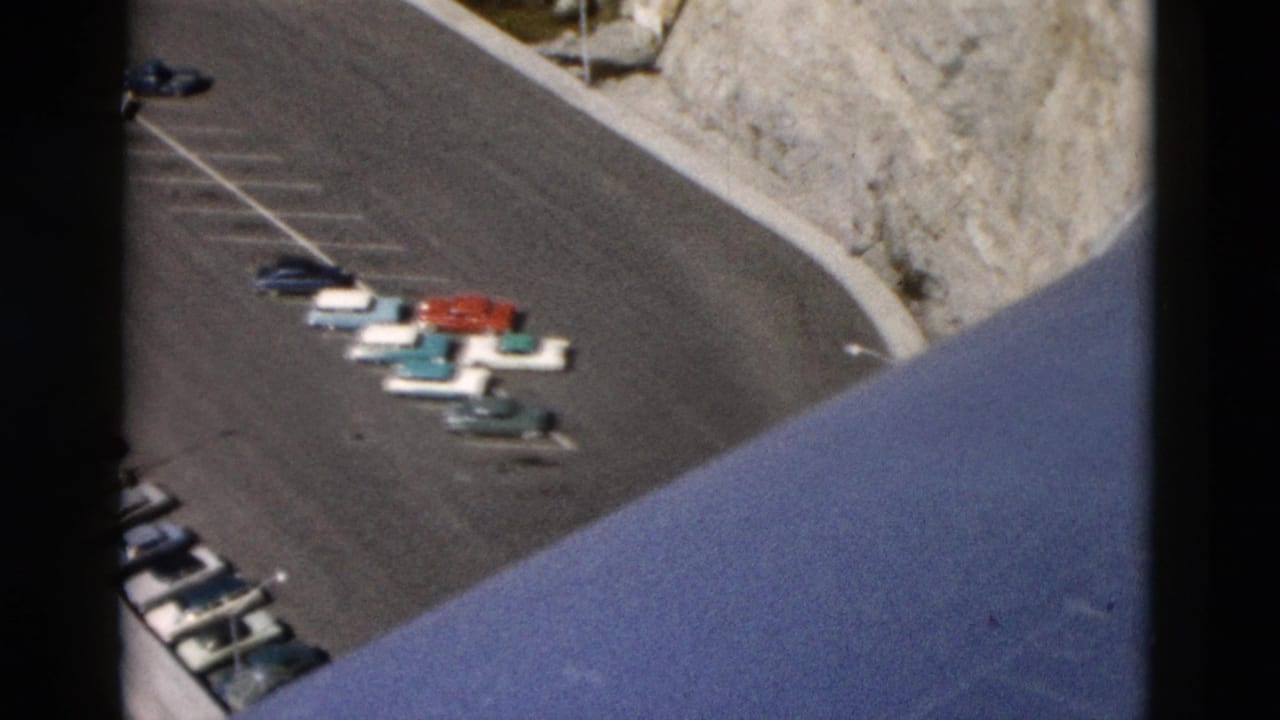 High-angle 8mm view of mid-century cars parked by a mountain road in the stated Montana travel scene.