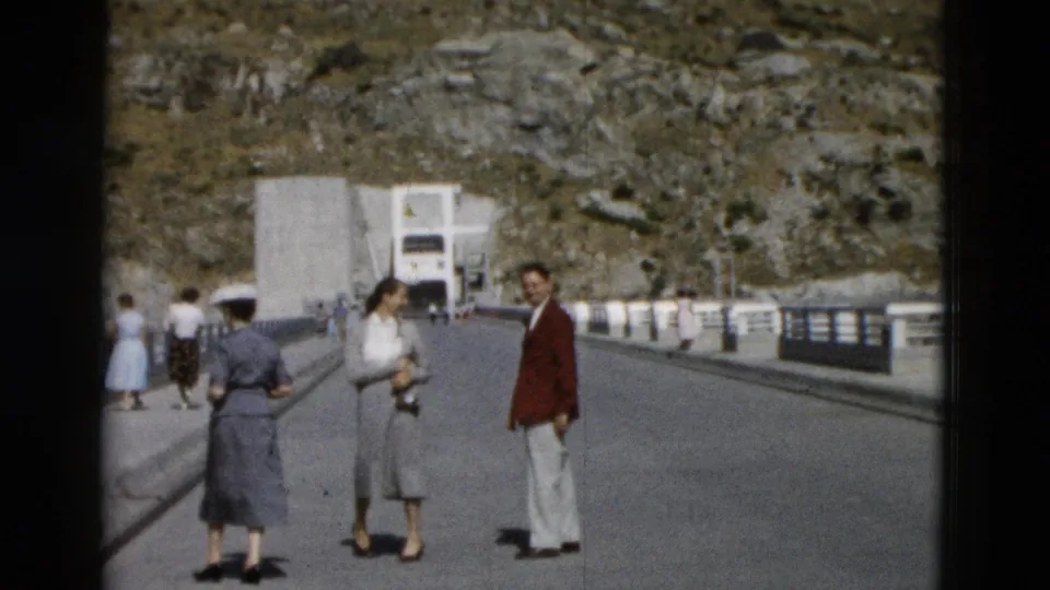 Montana 1958 bridge scene with a woman holding a camera and a man in a red jacket facing the home-movie camera.
